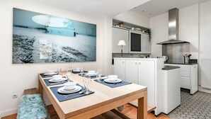 A modern kitchen with white cabinets, a stainless steel range hood, and a dining area with a wooden table set for four. - Urban Comfort: Central 2-BR Townhouse for 6 (Gent)