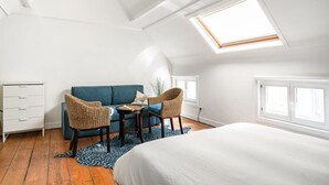 A bedroom with a skylight, a bed, a blue sofa, two wicker chairs, a small table, and a white dresser. - Urban Comfort: Central 2-BR Townhouse for 6 (Gent)