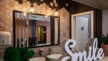 A bathroom with a hexagonal patterned wall, a large mirror, two sinks, and a 'Smile' sign.