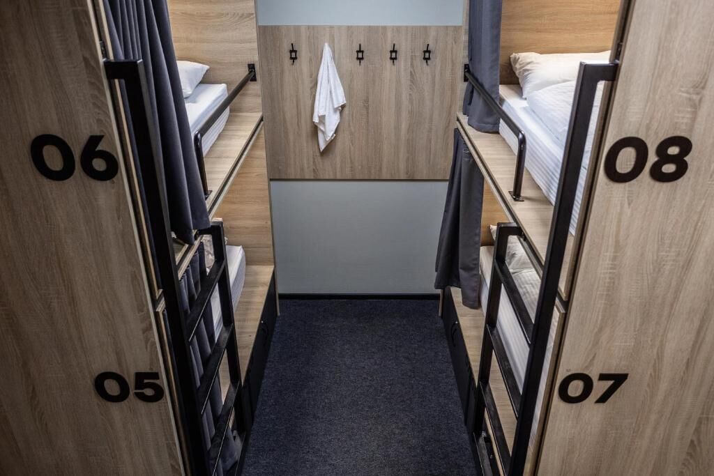 A narrow hallway with bunk beds numbered 05 to 08, a wooden wall, and a towel hanging on a hook.