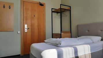 A bedroom with a wooden door, a bed with white linens, a hanging shoe rack, and a mirror.
