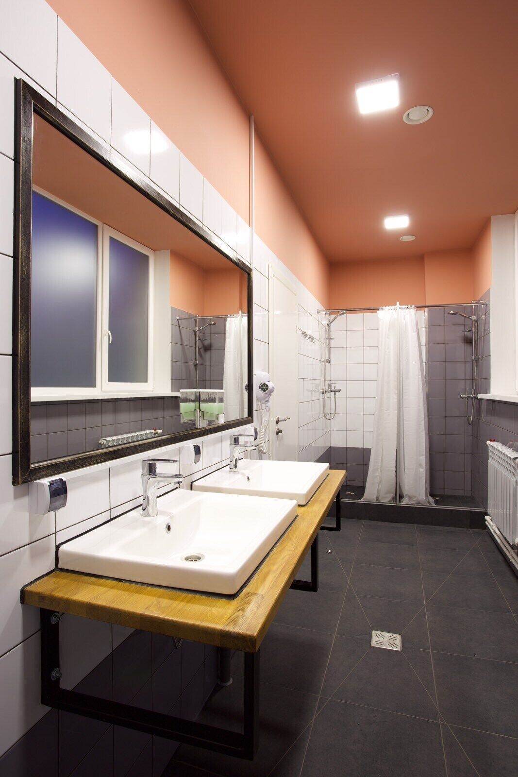 Ein modernes Badezimmer mit zwei Waschbecken, einer Ablage, einer Dusche und einem großen Spiegel.