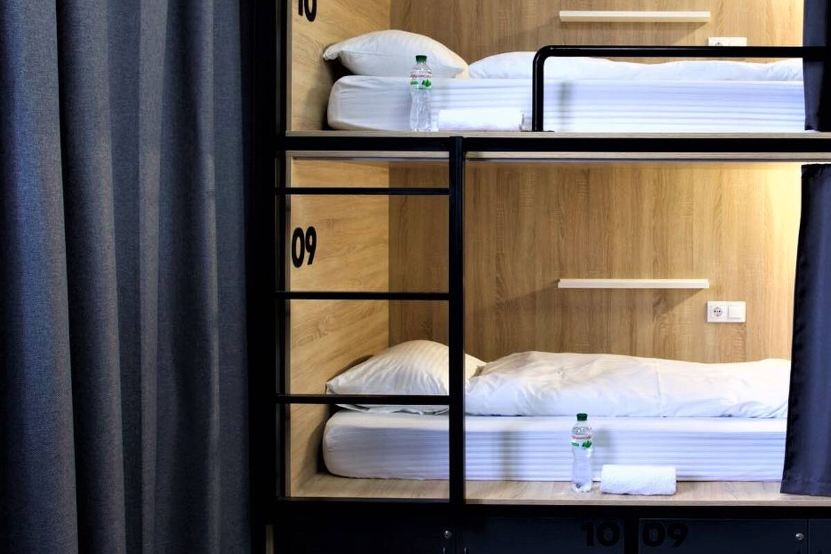 A bunk bed room with two beds, each labeled with a number. There is a small table and a power outlet on the wall.