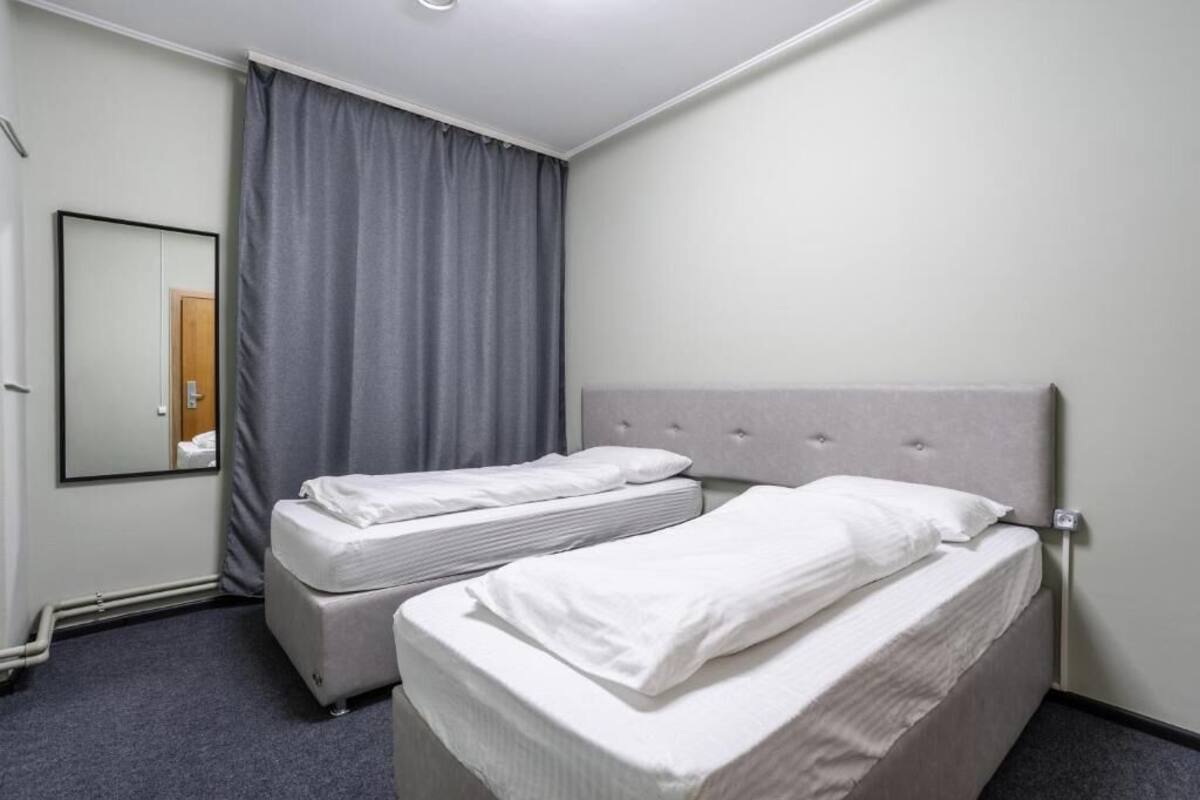 A hotel room with two single beds, a large mirror, and a grey curtain.