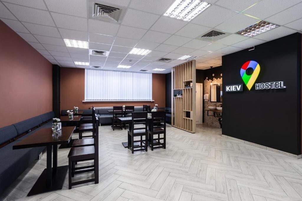 Interior moderno de un hostal con mobiliario de madera, una pared negra con un logotipo colorido y un patrón de suelo tipo espiga.