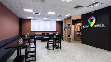 Interior moderno de un hostal con mobiliario de madera, una pared negra con un logotipo colorido y un patrón de suelo tipo espiga.