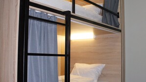 A bunk bed with a wooden frame, a lower bunk with a mattress and pillows, and a top bunk with a mattress and a blanket. There is a curtain on the lower bunk and a light fixture above the top bunk. - Kiev Hostel (Kyiv)