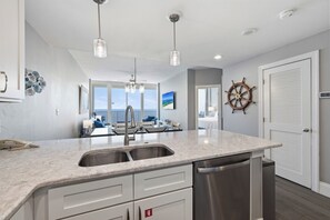 Una cocina moderna con una isla grande, electrodomésticos de acero inoxidable, iluminación colgante y vista al área de estar.