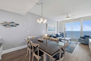 Een eethoek met een houten tafel en stoelen, een kroonluchter en uitzicht op de oceaan door grote ramen.
