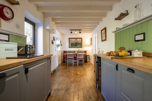 A kitchen with wooden flooring, white cabinets, a wooden countertop, and a dining area with a table and chairs.