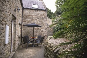 A stone building with a small patio area featuring a table and chairs under a black umbrella.