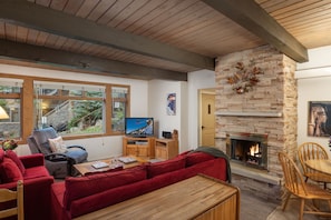A cozy living room with a fireplace, red sofas, a television, and a stone wall. - Aspenwood L2 - Ski, Soak, Relax | Cozy Mountain Stay, Walk to Slopes (Snowmass Village)
