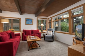 A living room with a red sofa, a grey armchair, a wooden coffee table, and a television on a wooden stand. - Aspenwood L2 - Ski, Soak, Relax | Cozy Mountain Stay, Walk to Slopes (Snowmass Village)