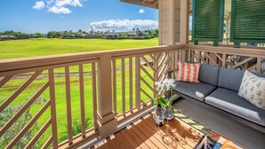 A balcony with a view of a golf course, a sofa, and a table with a vase and wine glasses. - Pili Mai Family Condo 6G, 2 Bedroom, 2 Bath, Plus Loft with Queen Murphy Bed (Koloa)