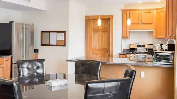 A modern kitchen with wooden cabinets, a dining area with a glass table, and a built-in oven. - 3BR/3BA + 3 Parking — Harvard/MIT, Red & Green Lines (Cambridge)