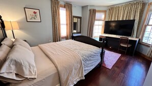 A hotel room with a bed, a desk with a TV, a chair, a lamp, and a window with curtains. - 3BR/3BA + 3 Parking — Harvard/MIT, Red & Green Lines (Cambridge)