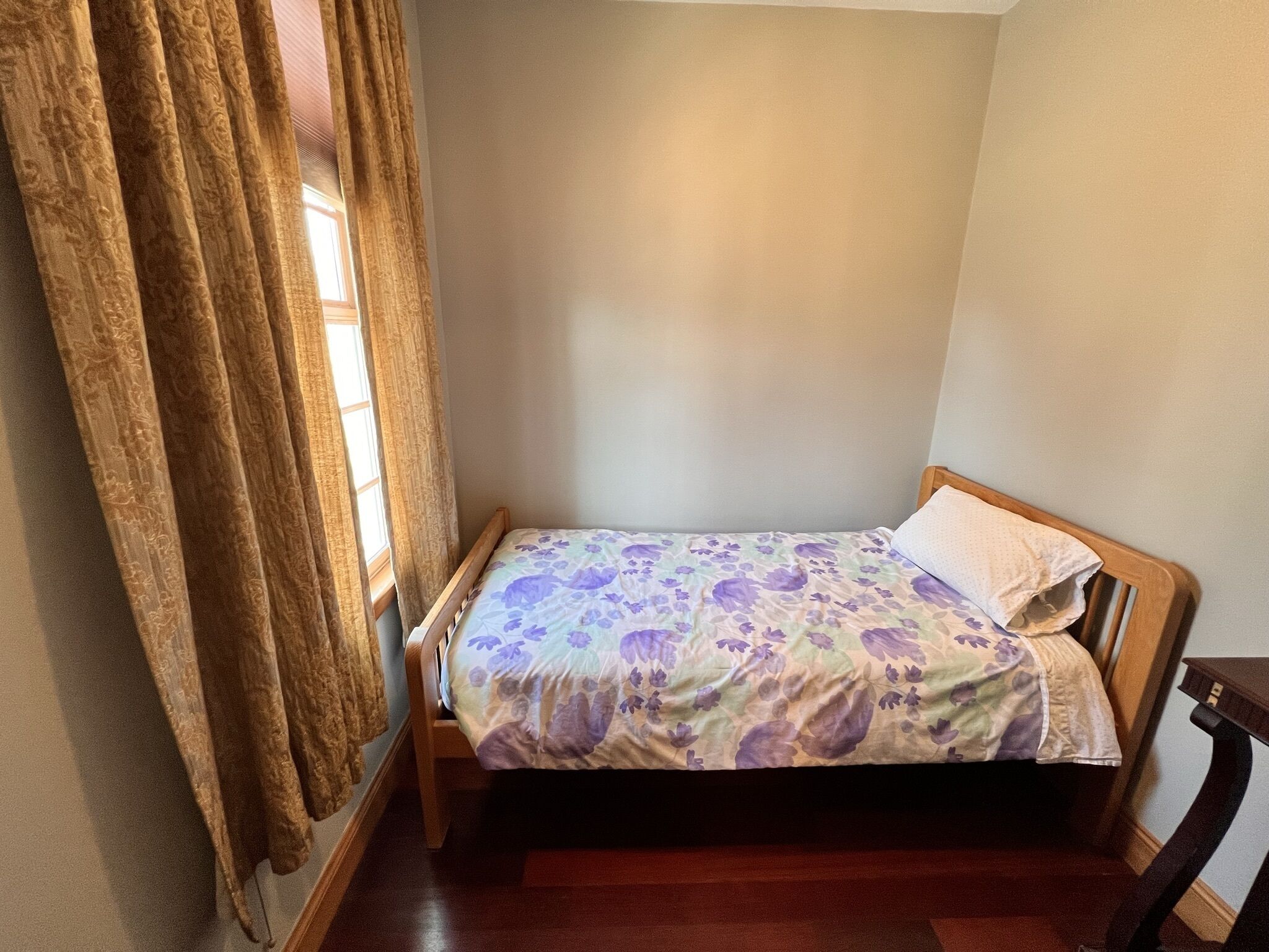 A small, single-bed room with a wooden frame and a floral bedspread.