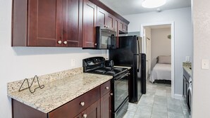 Una cocina compacta con armarios de madera oscura, encimera de granito, refrigerador negro y estufa.