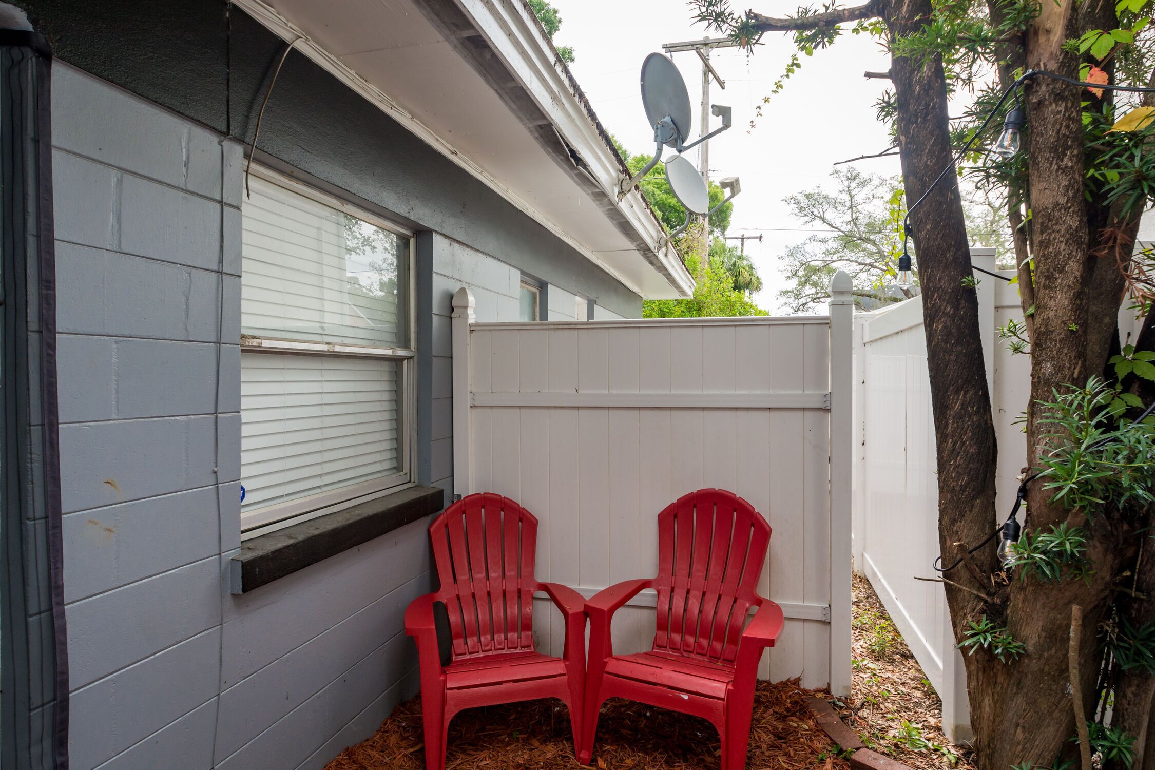 A small outdoor area with two red chairs, a white fence, and a satellite dish.