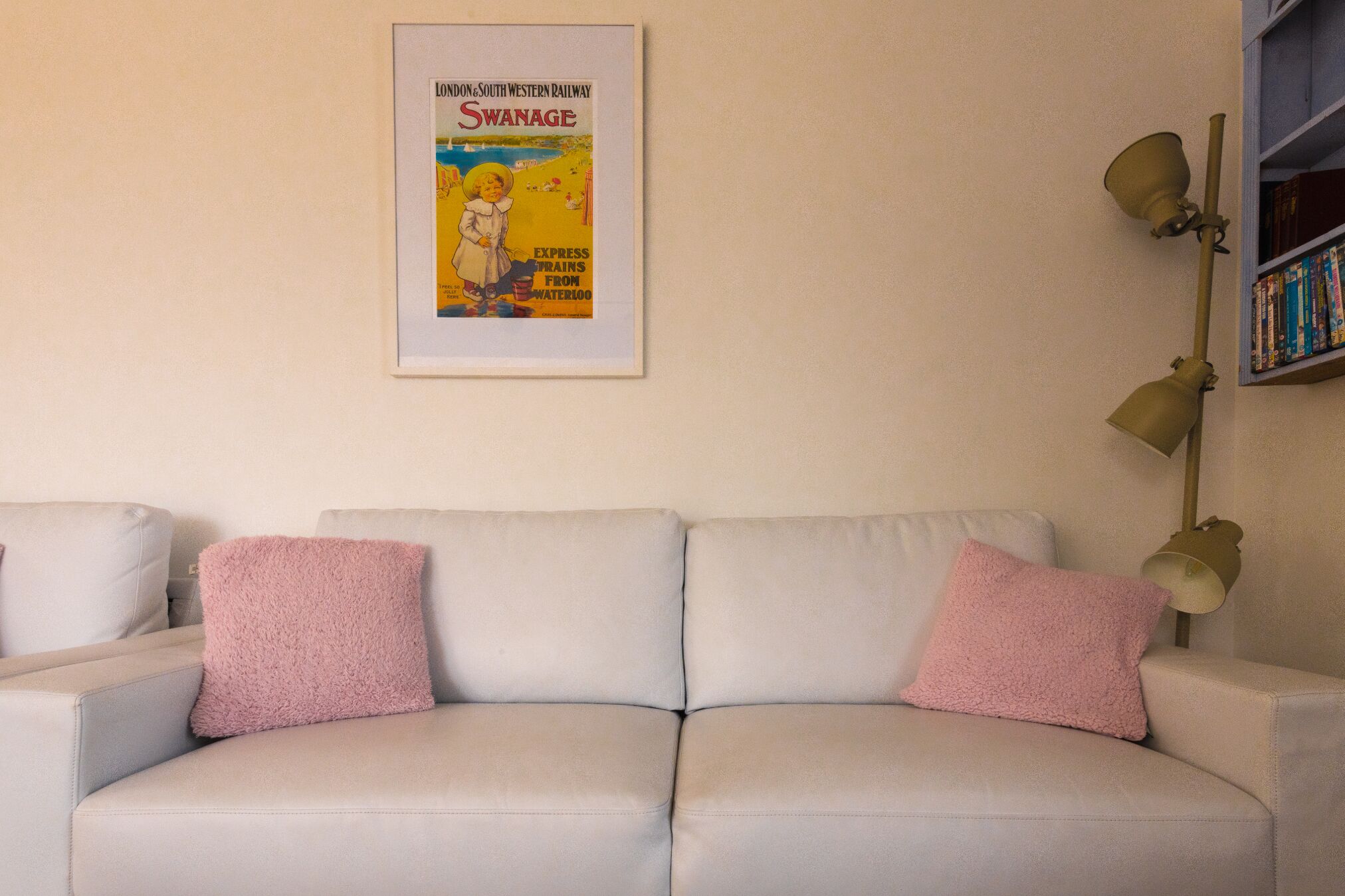 Un sofá blanco con almohadas rosadas y un cartel enmarcado de un tren en la pared.