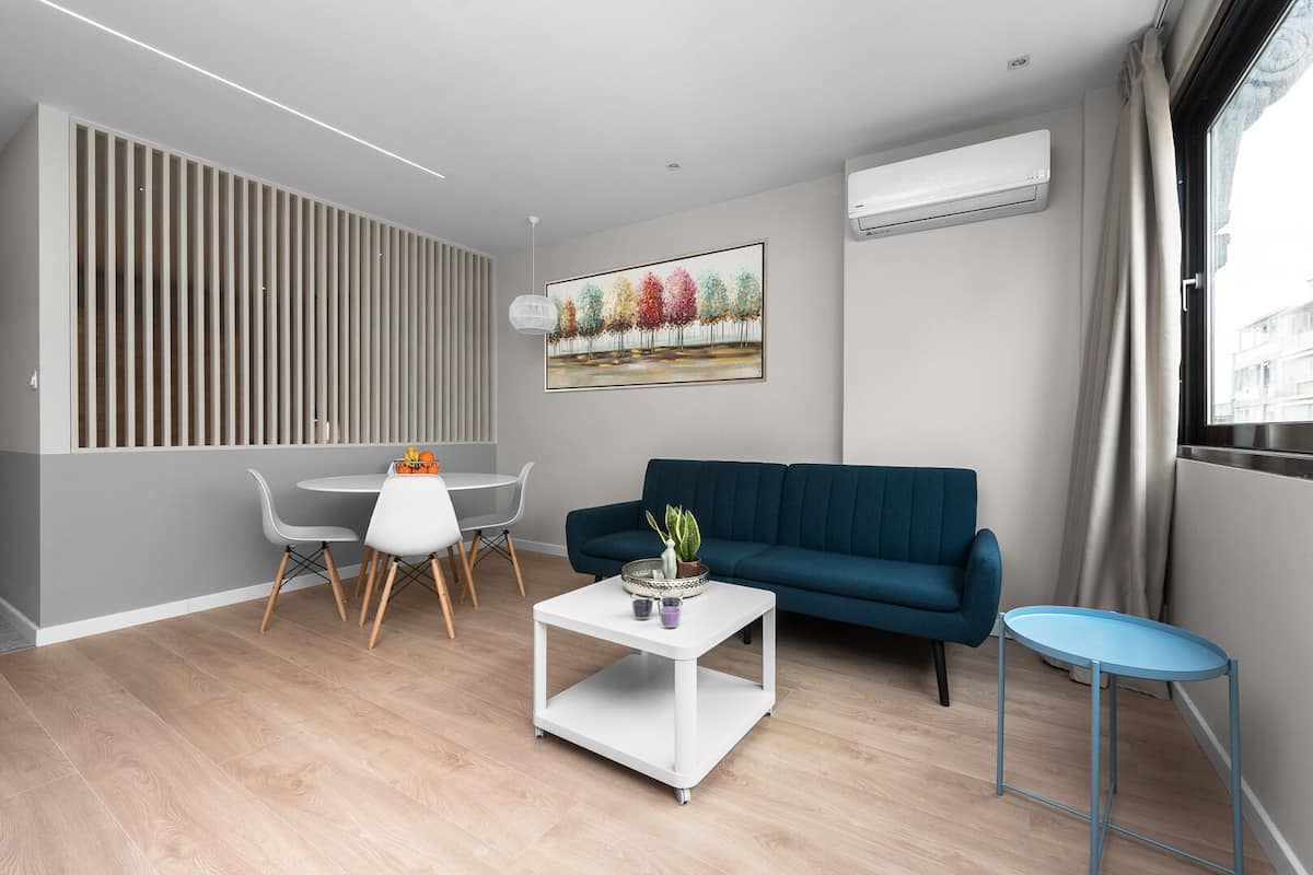 A modern living room with a blue sofa, a white coffee table, and a dining area with a white table and chairs.