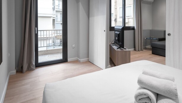 A modern hotel room with a large bed, a TV, and a balcony with a view of the city. - New Yorker Nilie Hospitality MGMT (Thessaloniki)