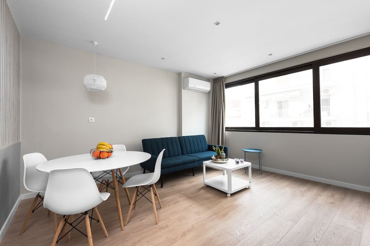 A modern living room with a round dining table, white chairs, a blue sofa, and a small side table with a plant.