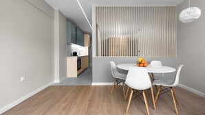 A modern kitchen with a built-in oven and a dining area with a round table and white chairs. - New Yorker Nilie Hospitality MGMT (Thessaloniki)