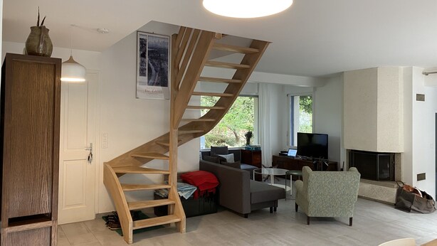 Ein modernes Wohnzimmer mit einer Wendeltreppe aus Holz, einem Kamin, einem Fernseher und einem Sofa.