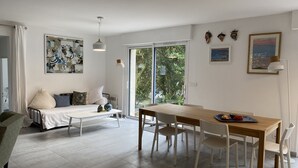 Ein modernes Wohnzimmer mit einer Couch, einem Esstisch mit Stühlen, einem großen Fenster und Bildern an den Wänden.