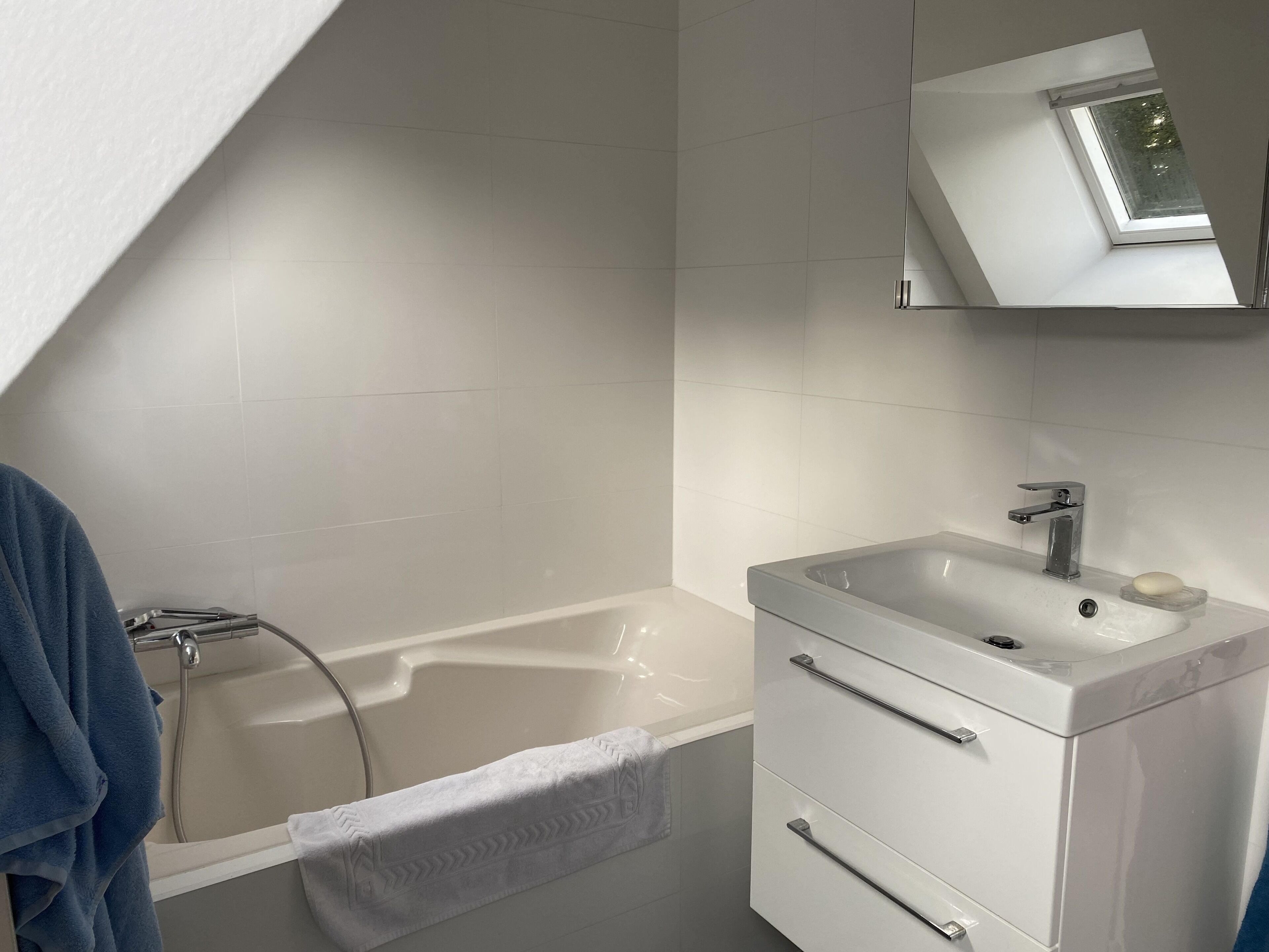 A modern bathroom with a freestanding bathtub, a vanity with a mirror, and a skylight above the tub.