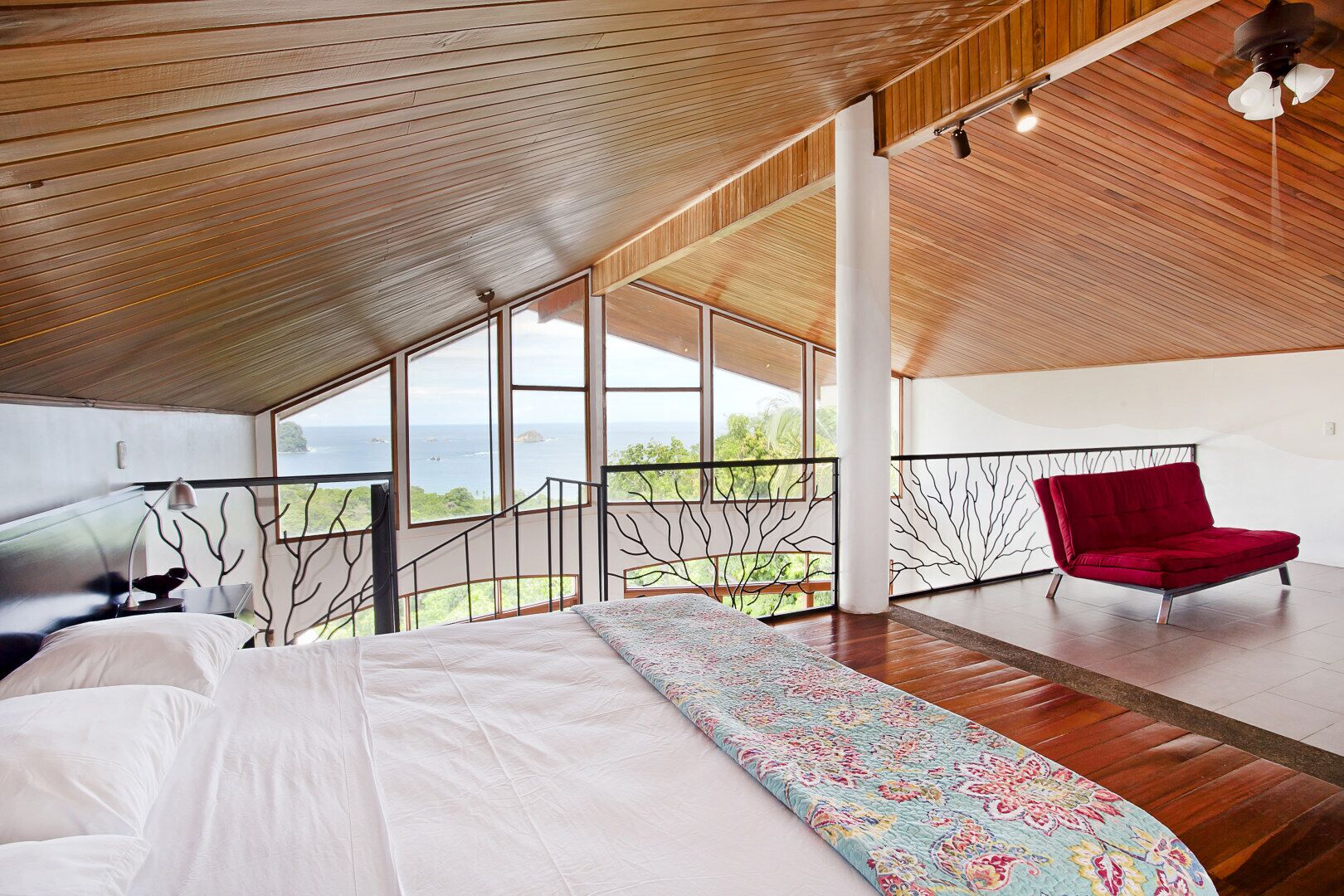 Une chambre avec un grand lit, un fauteuil rouge et un balcon donnant sur la mer.