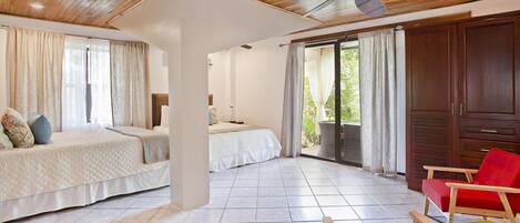 A hotel room with two beds, a red chair, a wooden ceiling, and a view of greenery outside.