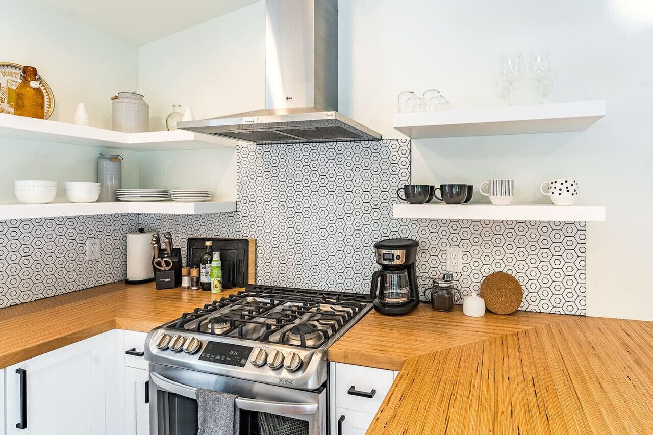 Een moderne keuken met een gasfornuis, koffiezetapparaat en diverse keukengerei op planken.