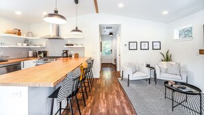 A modern kitchen with a wooden island, pendant lights, and a view into a living area with a sofa and chairs. - Midtown gem I Park view I Full kitchen (Bend)