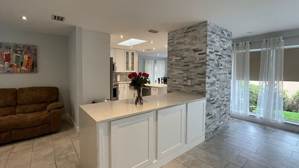 A modern kitchen with white cabinets, a stone accent wall, and a large window with sheer curtains. - Bright & Spacious Villa in Hollywood ★ 3BR/2BA ★ Heated Pool ★Walk to Beach (hollywood)