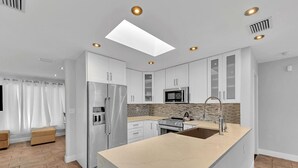 A modern kitchen with white cabinets, a stainless steel refrigerator, a microwave, and a large island with a sink. - Bright & Spacious Villa in Hollywood ★ 3BR/2BA ★ Heated Pool ★Walk to Beach (hollywood)