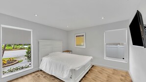 A bedroom with a large window, a bed, a bedside table, and a mounted TV. - Bright & Spacious Villa in Hollywood ★ 3BR/2BA ★ Heated Pool ★Walk to Beach (hollywood)