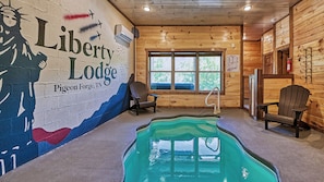 A cabin interior with a pool, Adirondack chairs, and a mural of a person holding a torch.
