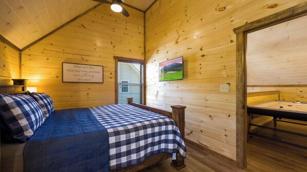 A wooden cabin room with a bed, a painting, and a sign on the wall.