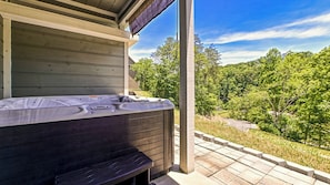 A hot tub on a wooden deck with a view of a forested area.