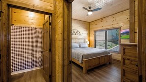 Ein Schlafzimmer einer Holzhütte mit Bett, Fenster, Deckenventilator und einer karierten Duschvorhang.