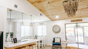 A modern kitchen with wooden ceiling, pendant lights, a central island, and a dining area with white chairs. - Riverfront Cottage Retreat with 2 Docks + Scenic Views on the St. John’s River! (Satsuma)