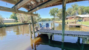 A wooden dock extending over a calm body of water, with a clear view of a grassy area and trees in the background. - Riverfront Cottage Retreat with 2 Docks + Scenic Views on the St. John’s River! (Satsuma)