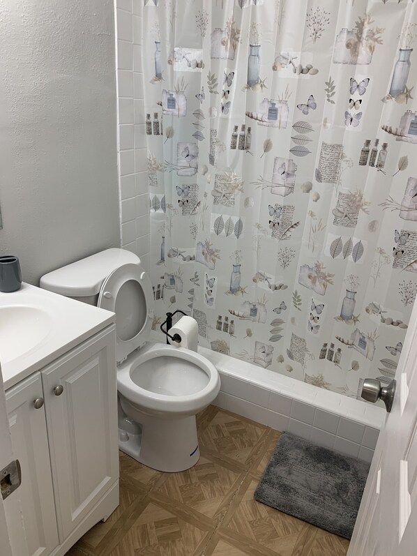 A bathroom with a toilet, bidet, and sink. It has a shower curtain with a nature-themed pattern. - 3x2 Home 10/15 minutes from Universal/Disney (Orlando)