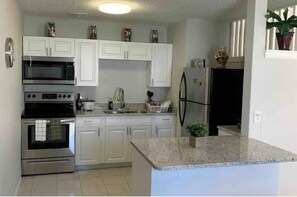 A modern kitchen with white cabinets, stainless steel appliances, and a granite countertop. - 3x2 Home 10/15 minutes from Universal/Disney (Orlando)
