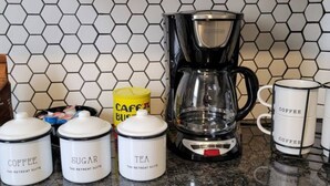 En köksbänk med en kaffebryggare, behållare för socker och te samt en kaffemugg.