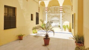 A courtyard with yellow walls, potted plants, and a stone archway. - Homey Seville. Duplex with Terrace in Santa Cruz, Sleeps 5, Parking Optional (Sevilla)