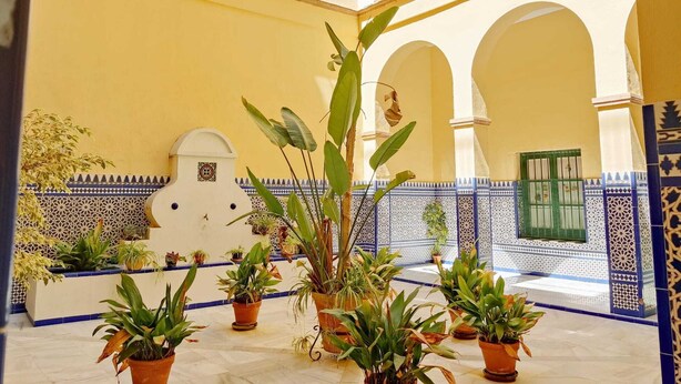 A courtyard with potted plants, tiled walls, and arches. - Homey Seville. Duplex with Terrace in Santa Cruz, Sleeps 5, Parking Optional (Sevilla)