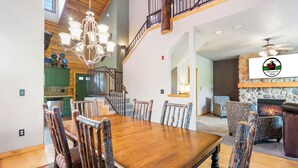 A spacious dining area with a wooden table and chairs, a chandelier, and a staircase leading to an upper level. - Spacious Cabin in the Heart of Branson, near shows, shopping! (Branson)